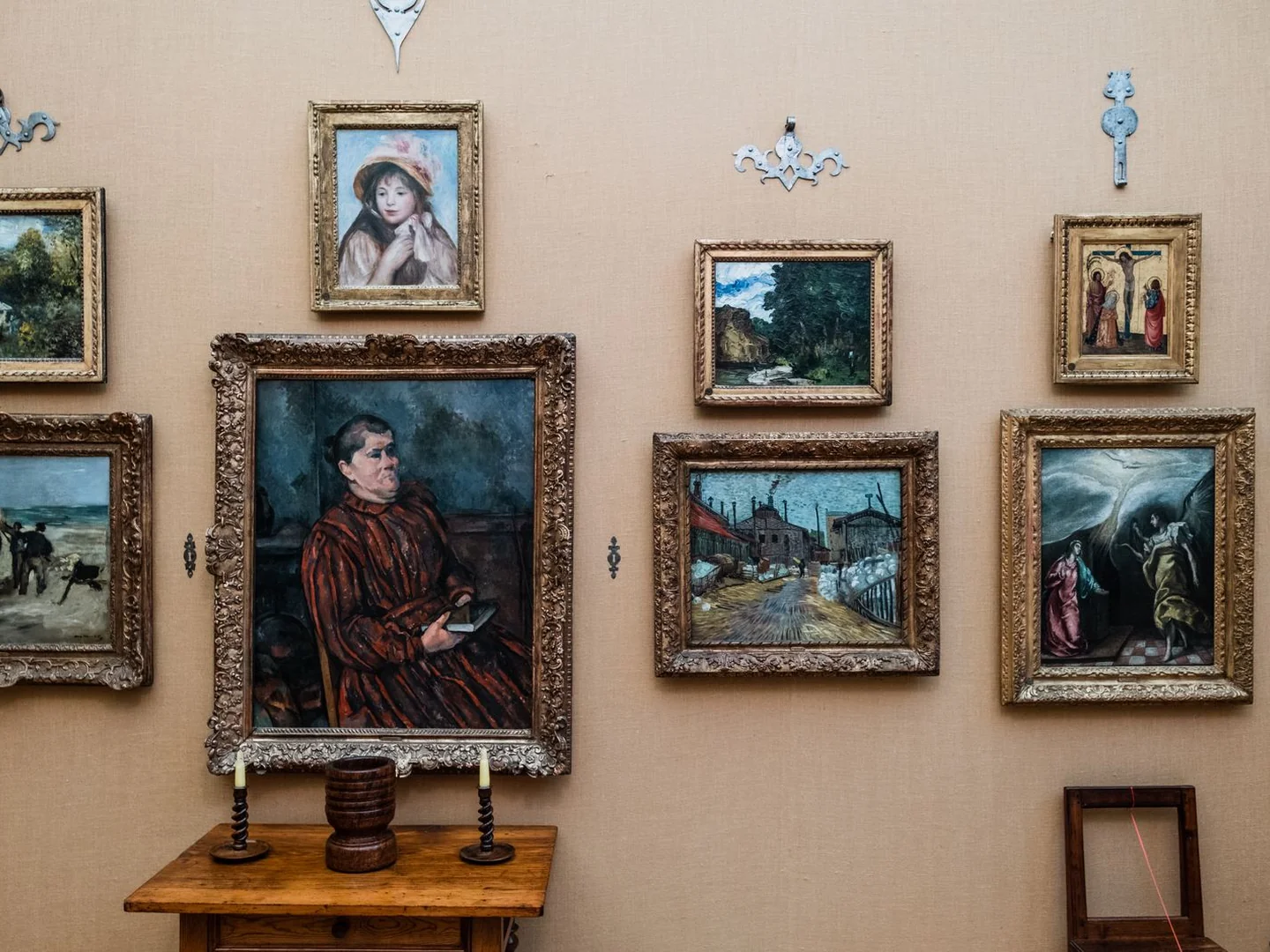 A mixed group of framed paintings on a muted beige wall.