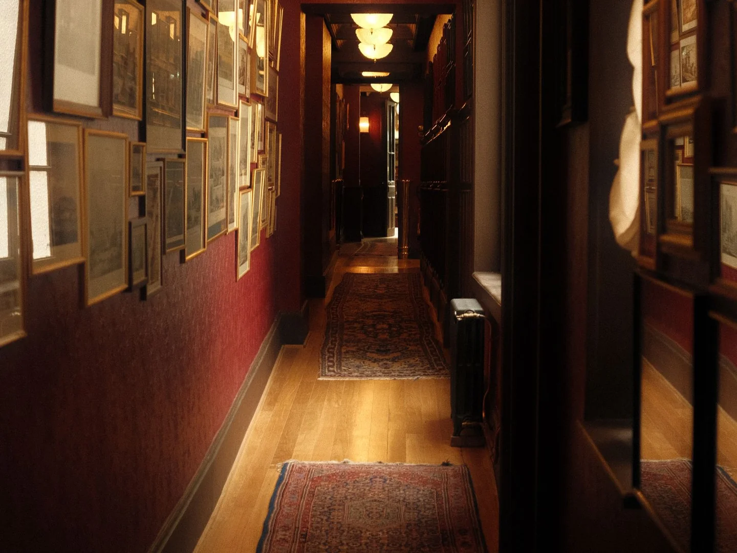 A long hallway with red lower walls, framed pictures and timber flooring.