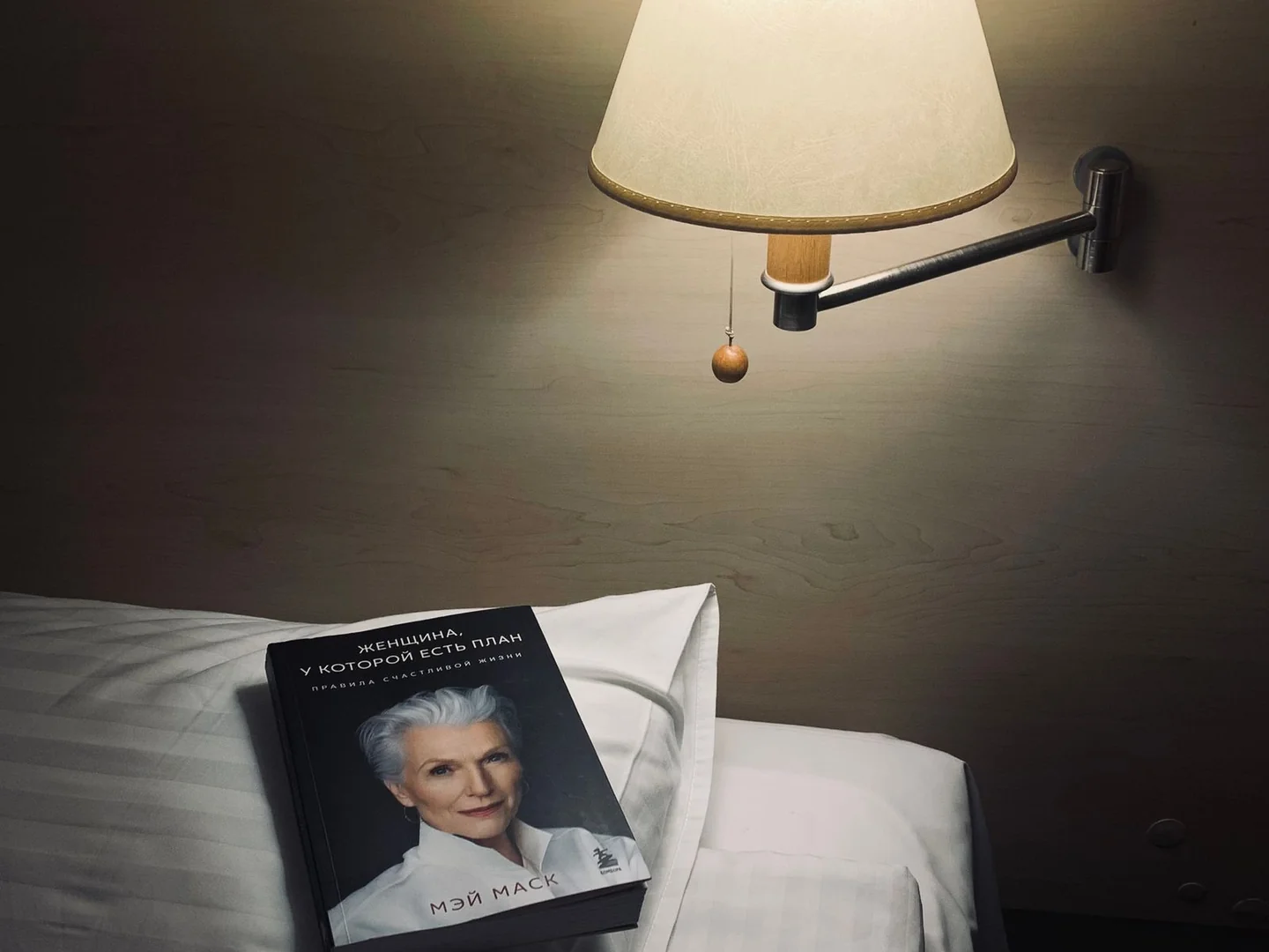 A bedside lamp with a pull switch above a book and pillow.