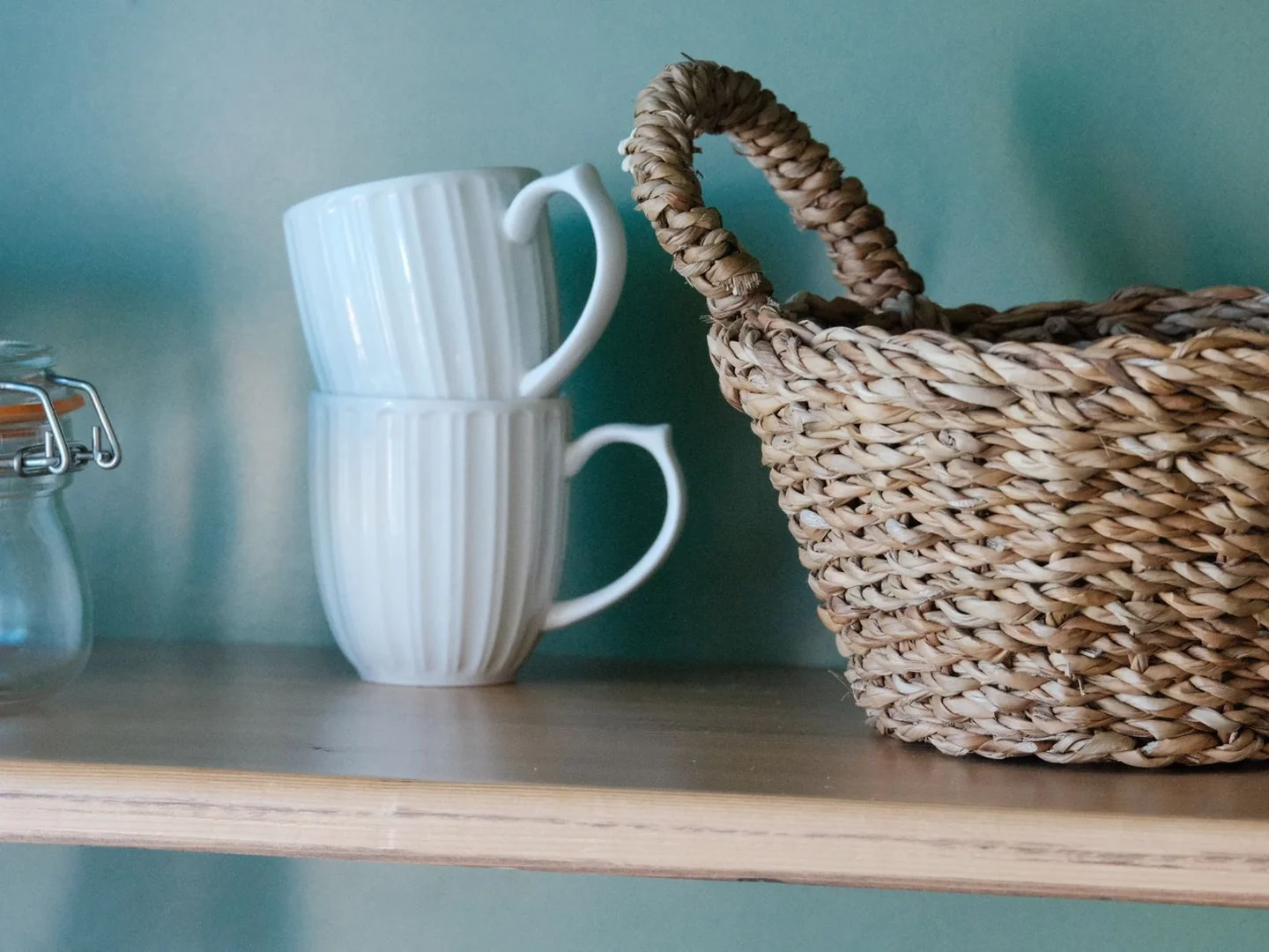 A woven basket and mugs on a shelf.