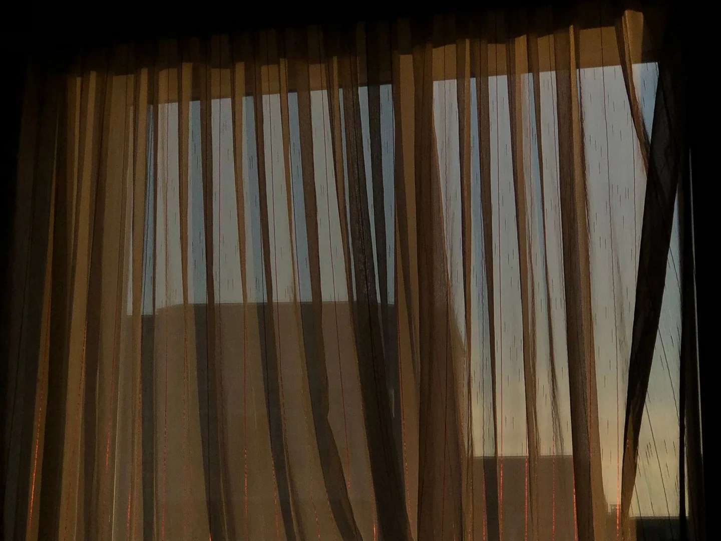 Daylight passing through translucent curtains across a window.