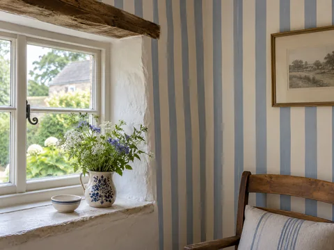 soft cream and blue striped wallpaper beside an old cottage window.
