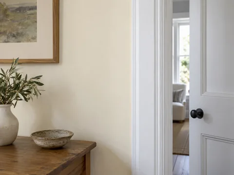 warm ivory painted wall beside a cooler white door frame, neutral interior detail.