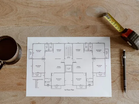 A floor plan on a table with a tape measure and pencil.