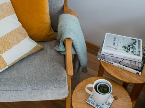 A small side table with a cup and books beside an upholstered armchair.