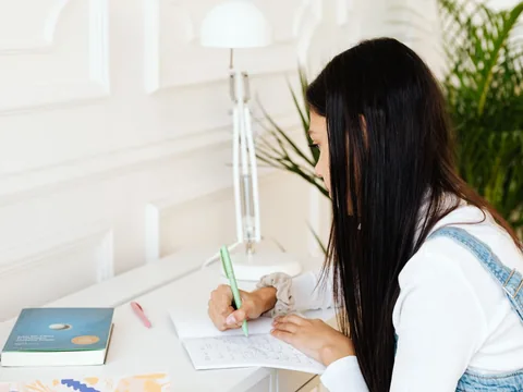 An adjustable desk lamp beside a notebook on a white desk.