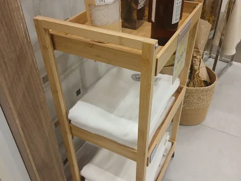 An open wooden bathroom shelf holding folded towels.