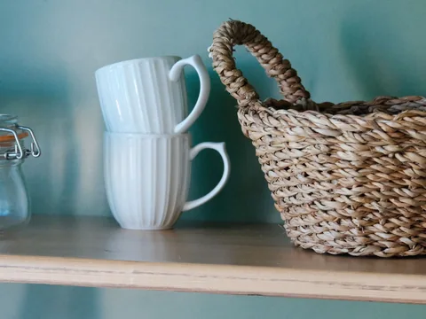 A woven basket and mugs on a shelf.