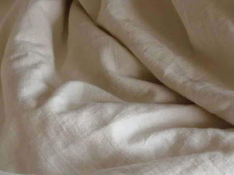 The creased surface of pale natural linen bedding.